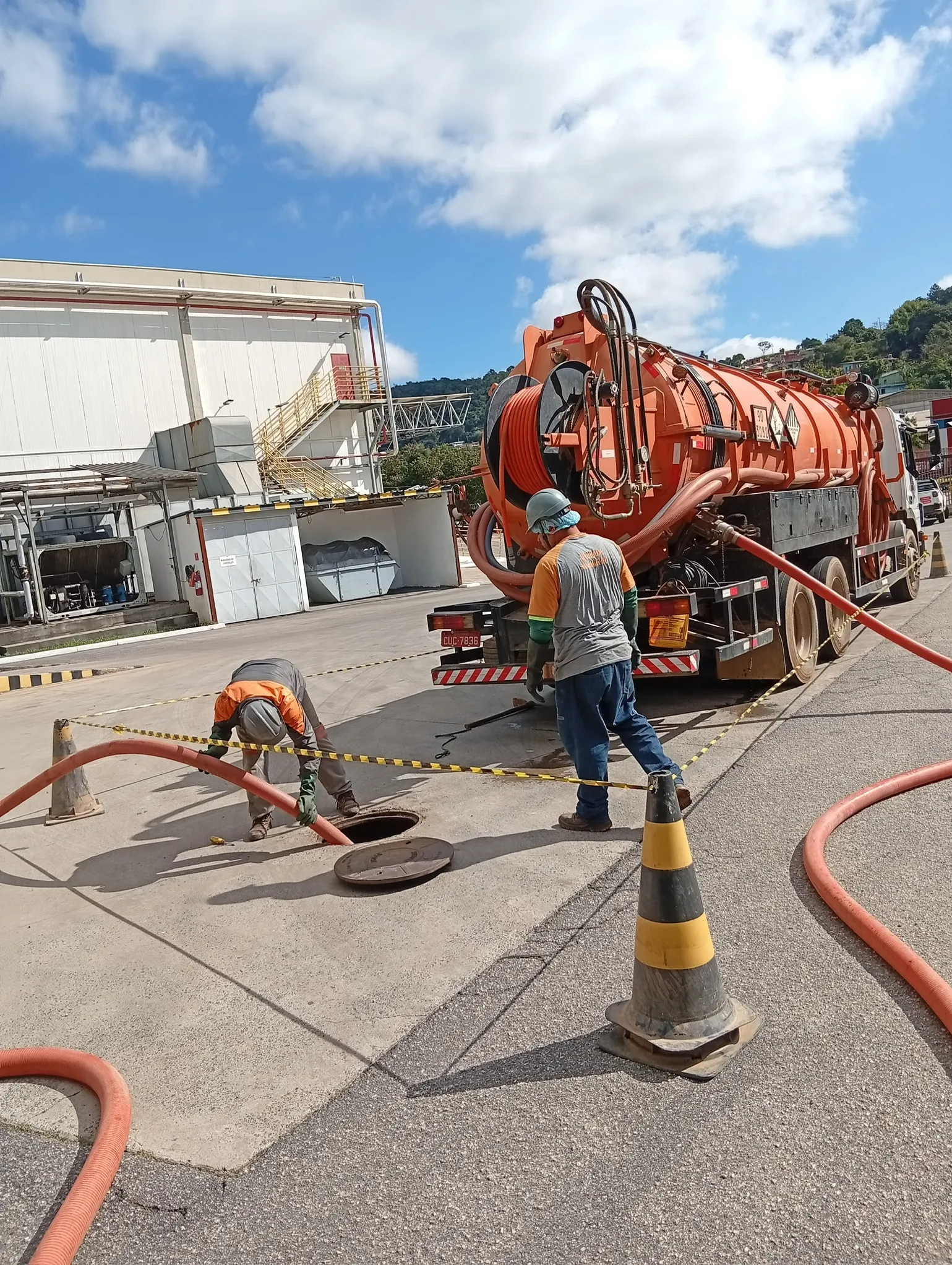 Equipe da Alvorada Saneamento abrindo poço de visita para limpeza com caminhão auto vácuo em área industrial, com cones e fita de sinalização isolando o perímetro